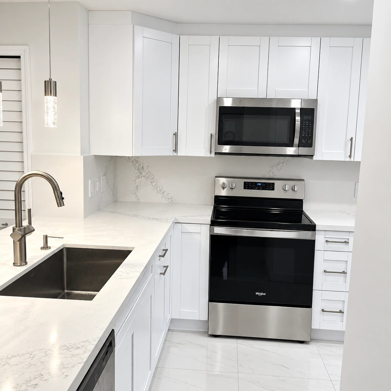 Detalle de la cocina blanca: fregadero bajo encimera, estufa y microondas de acero, backsplash de cuarzo y lavaplatos